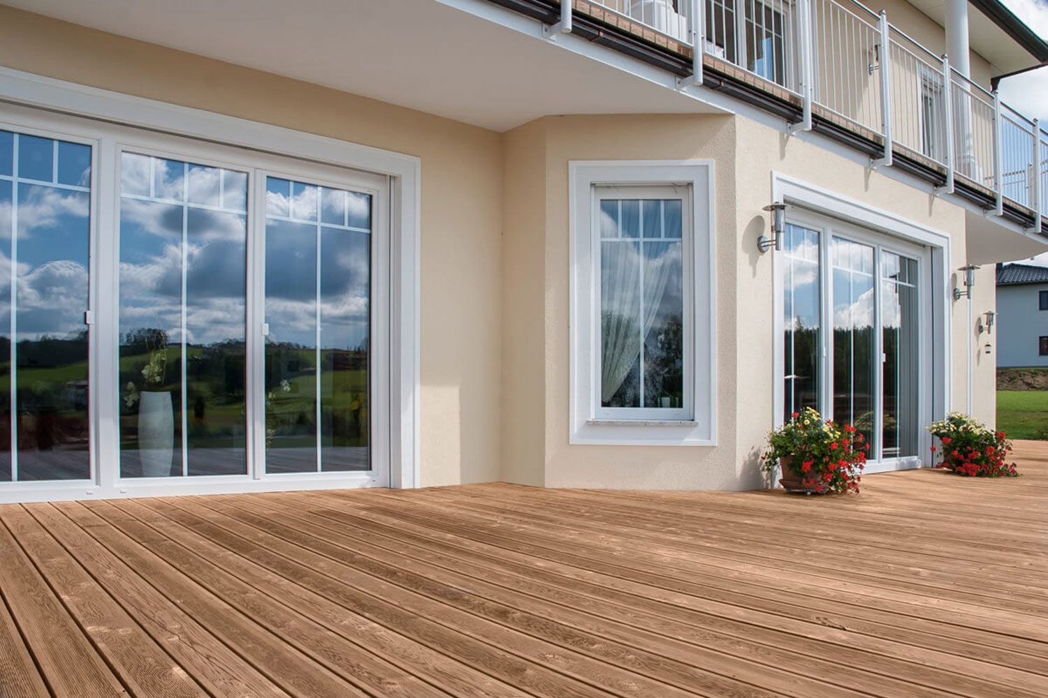 Esterno di una casa con ampie finestre e una terrazza in legno, inondata di luce solare.