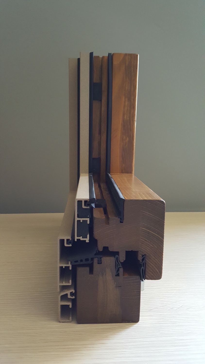 Sezione trasversale di un telaio di finestra in legno e alluminio, che ne evidenzia gli strati e la struttura con legno scuro e chiaro.