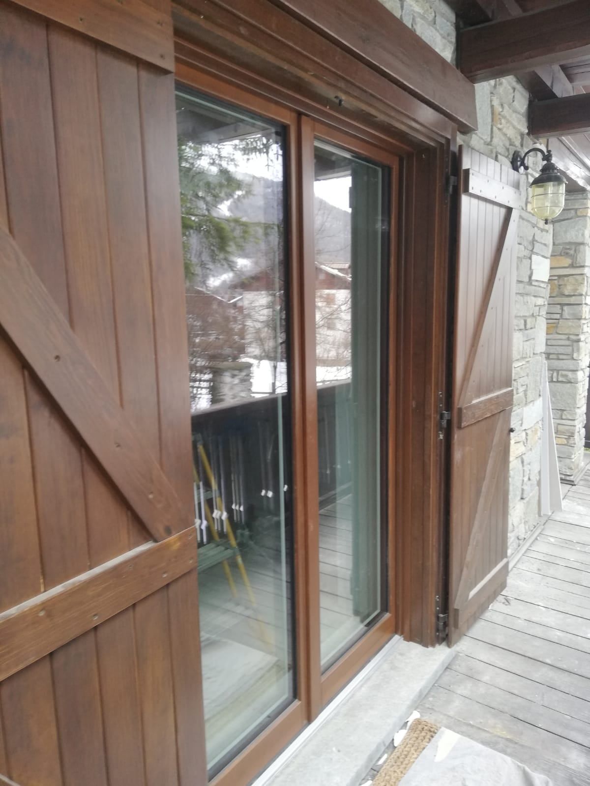 Persiane in legno e porta a vetri su un balcone con pareti in pietra.