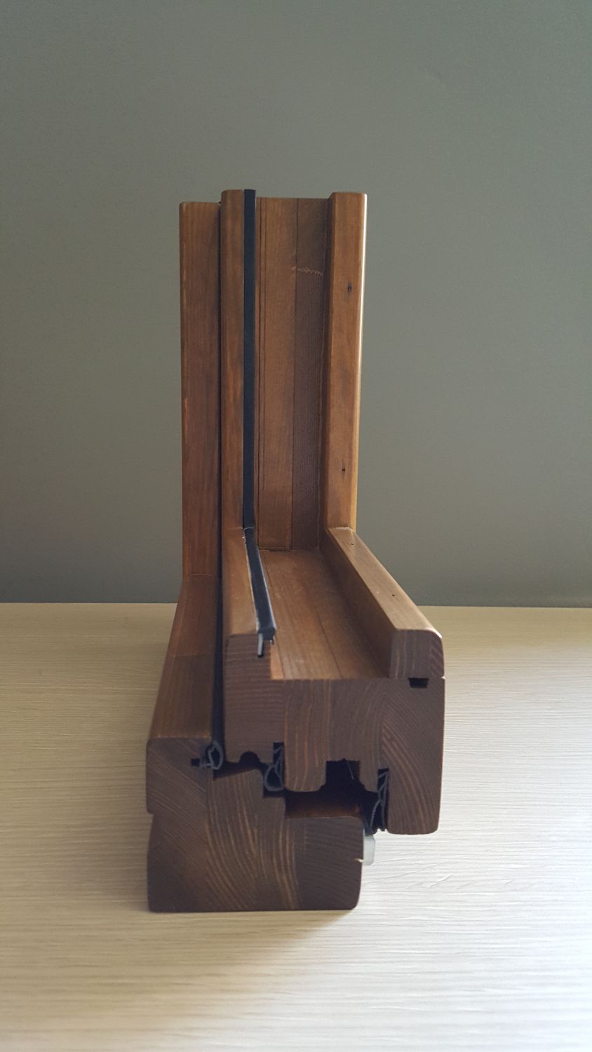 Sezione trasversale di un telaio di finestra in legno, che mostra la struttura a strati con scanalature e sigillante nero.