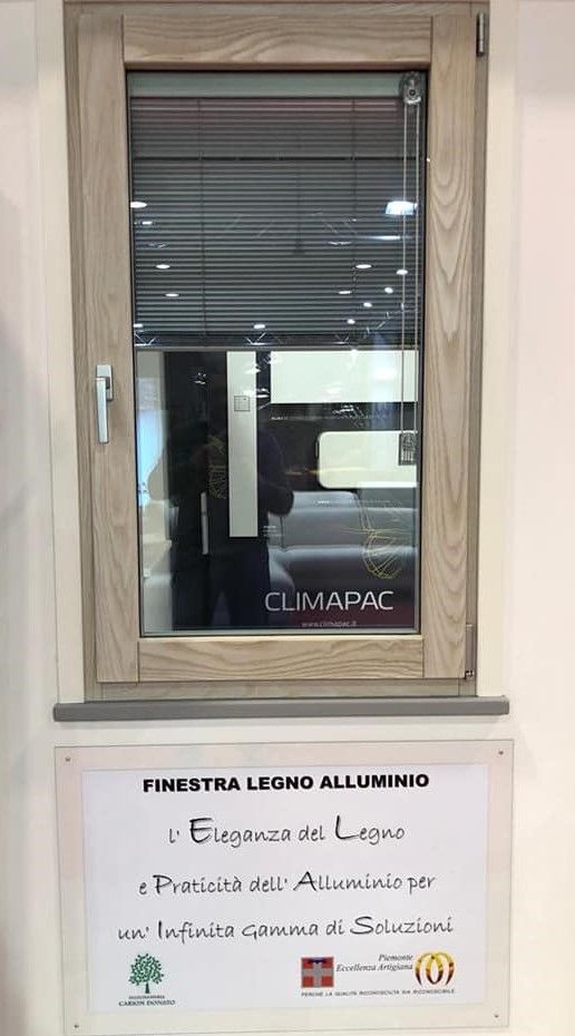 Finestra con telaio in legno e persiane integrate. Un cartello in basso pubblicizza