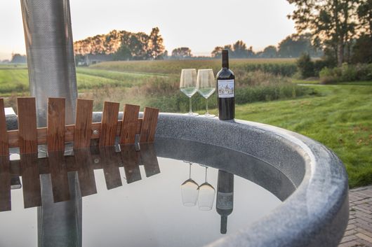 Een fles wijn en twee wijnglazen staan bij een hot tub.
