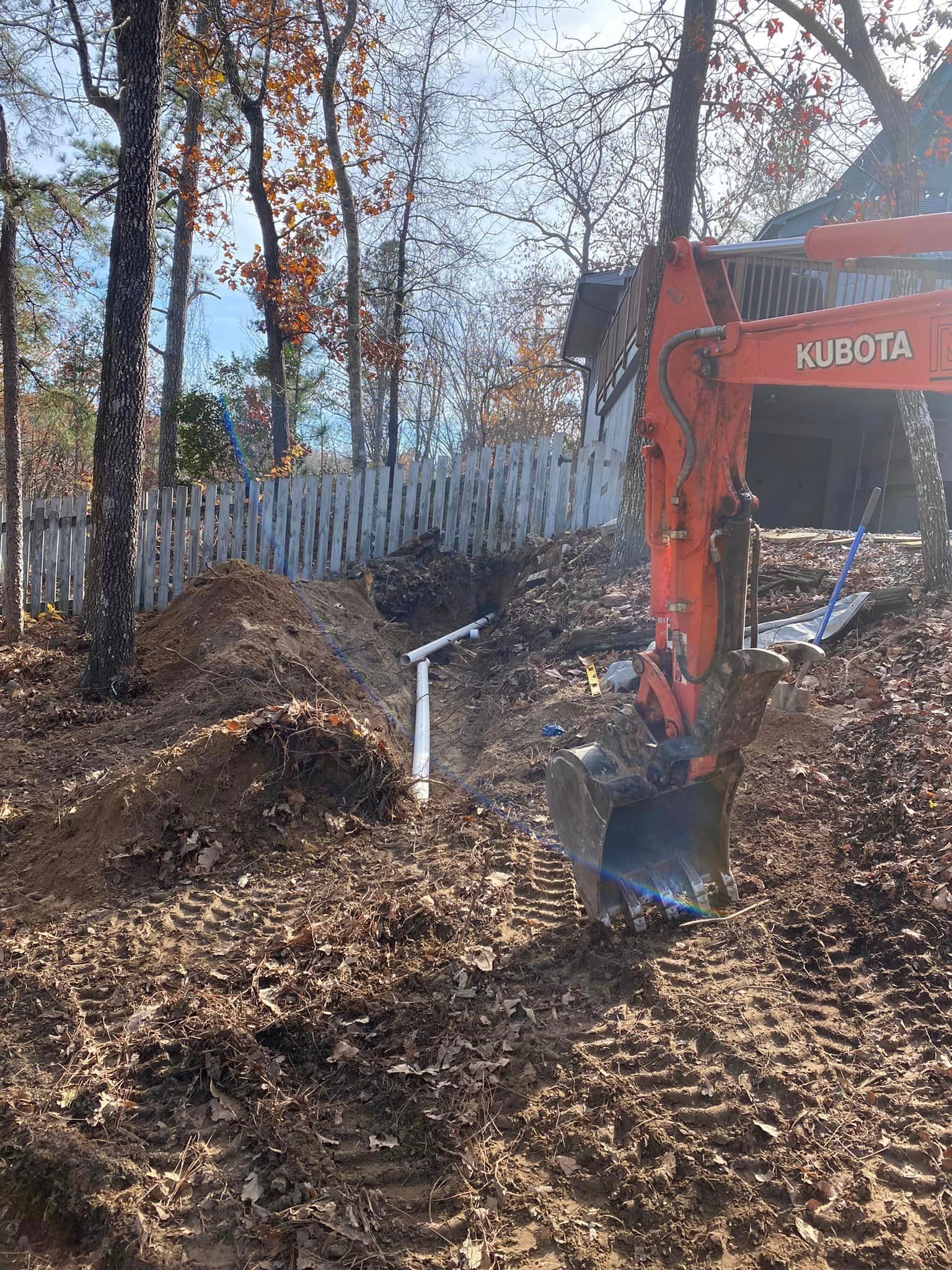 A kubota excavator is digging a hole in the ground in the woods.