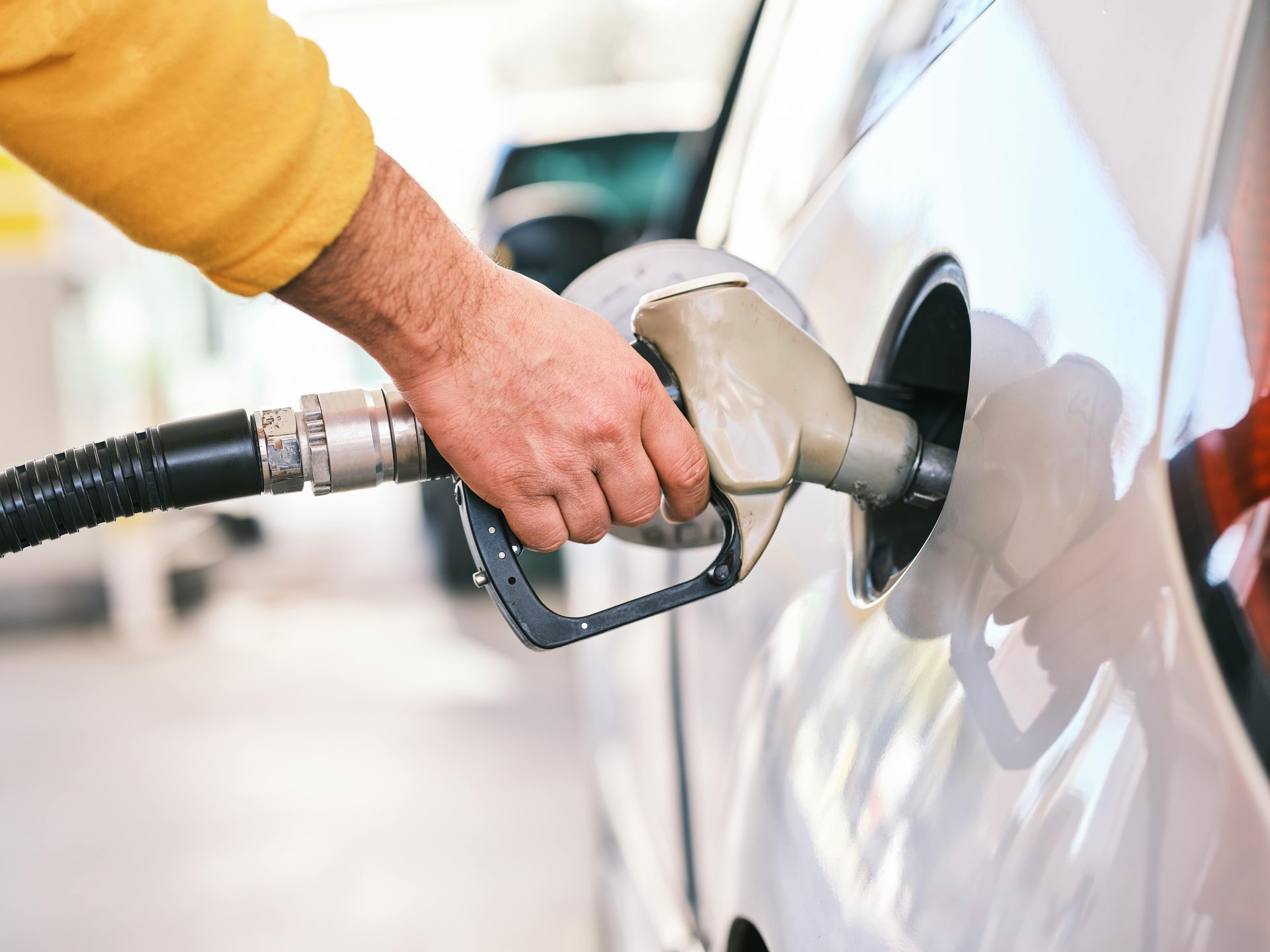 Person holding a fuel nozzle while refueling a white car at a gas station