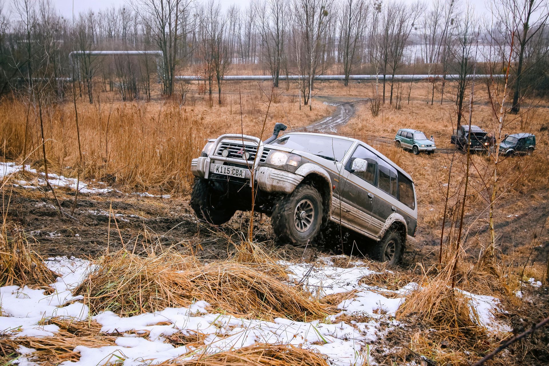 Off-road SUV climbing a muddy, snow-dusted embankment in a field