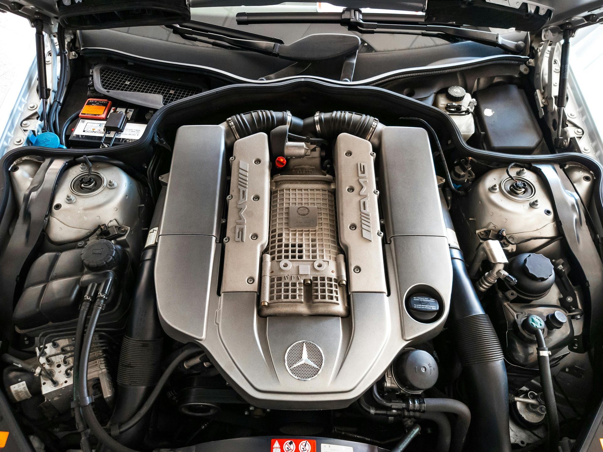 Close-up of a car engine bay with a silver engine cover and hoses under the hood.
