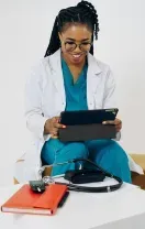 Healthcare worker in teal scrubs with headset, speaking at a desk with laptop and stethoscope