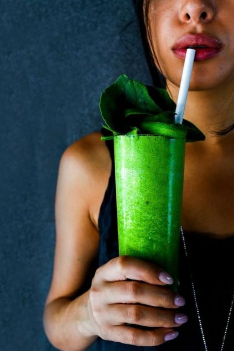Person holding a bright green smoothie with mint and a straw against a dark background