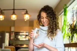Woman in a cozy kitchen examining a glass in her hand, smiling under warm pendant lights