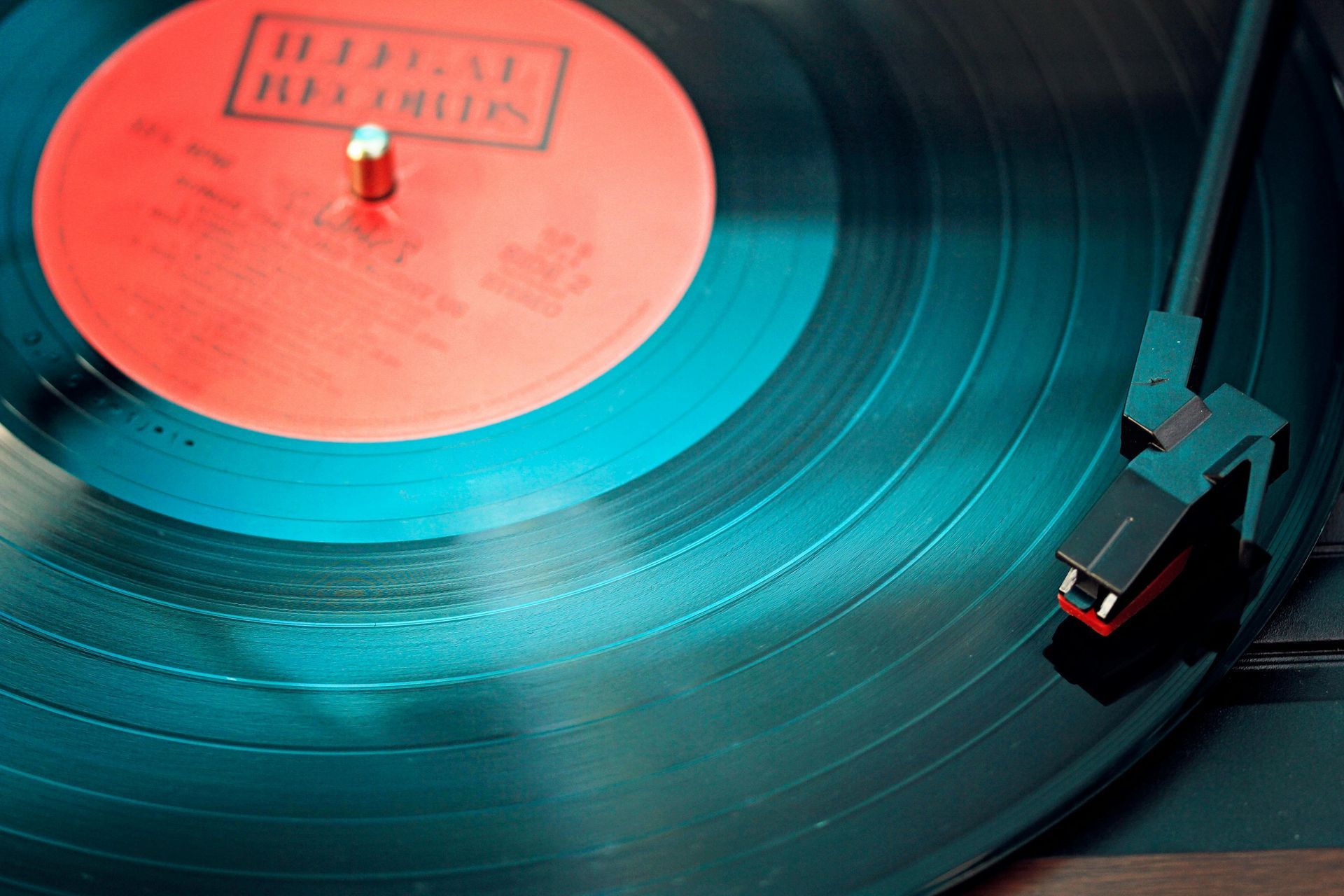 A record player with a black vinyl record, red label, and a needle playing music.