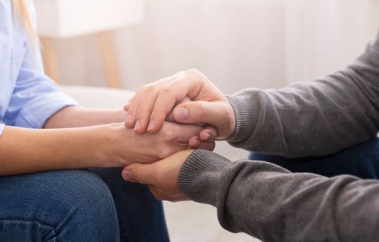 Due persone che si tengono per mano in un gesto di sostegno su un divano