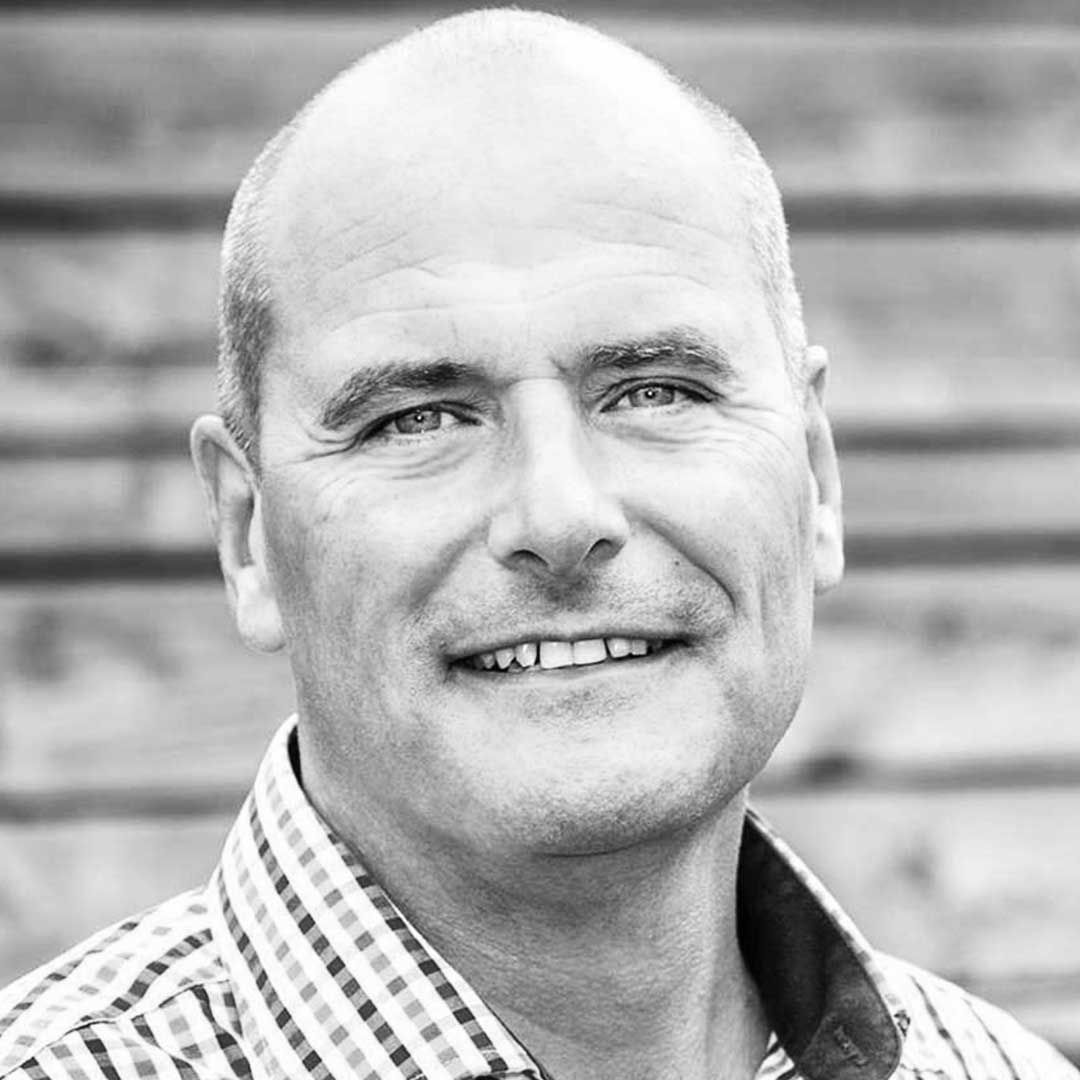 Et billede af Ulrik i en skjorte smiler på et sort-hvidt foto.