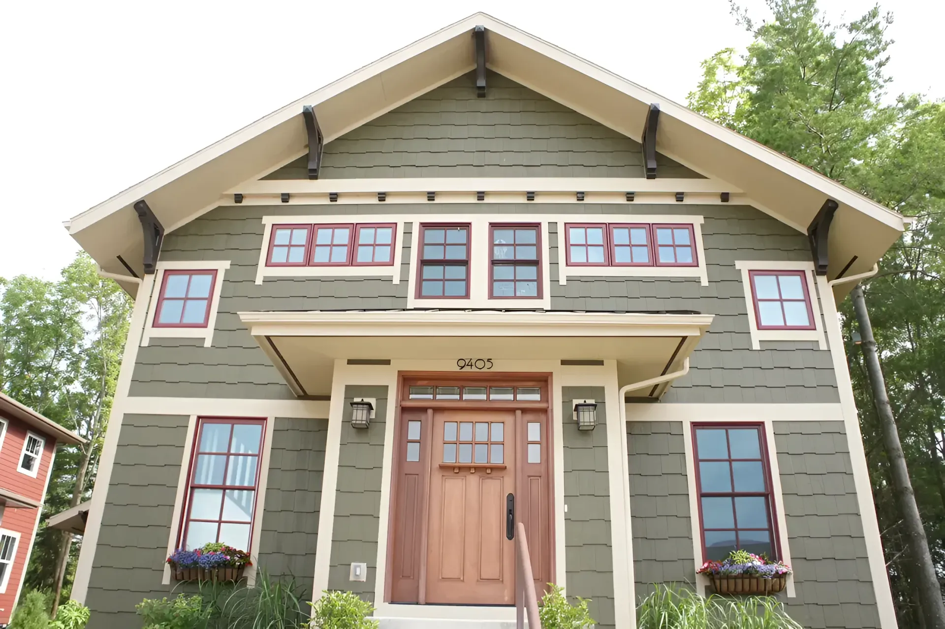 Front view of a gray-green house with brown trim, large windows, and a peaked roof.
