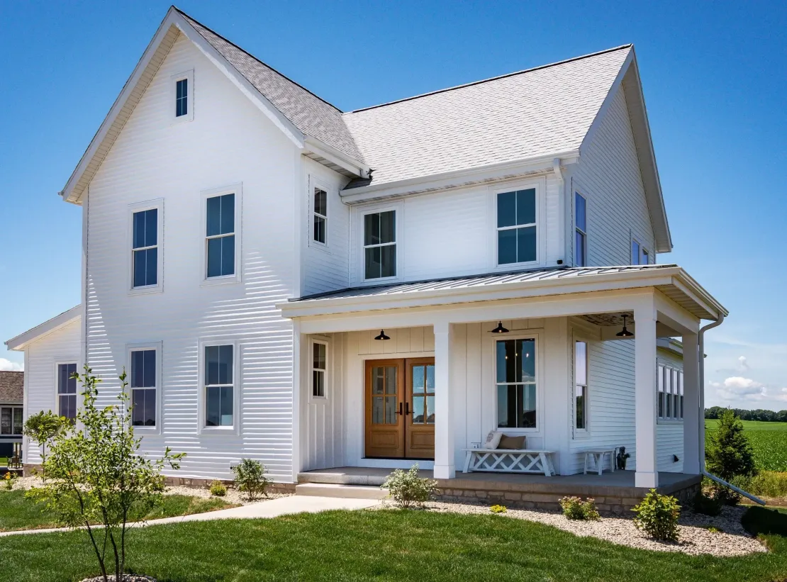 White two-story house with a front porch, blue shutters, and a well-kept lawn in bright sunlight