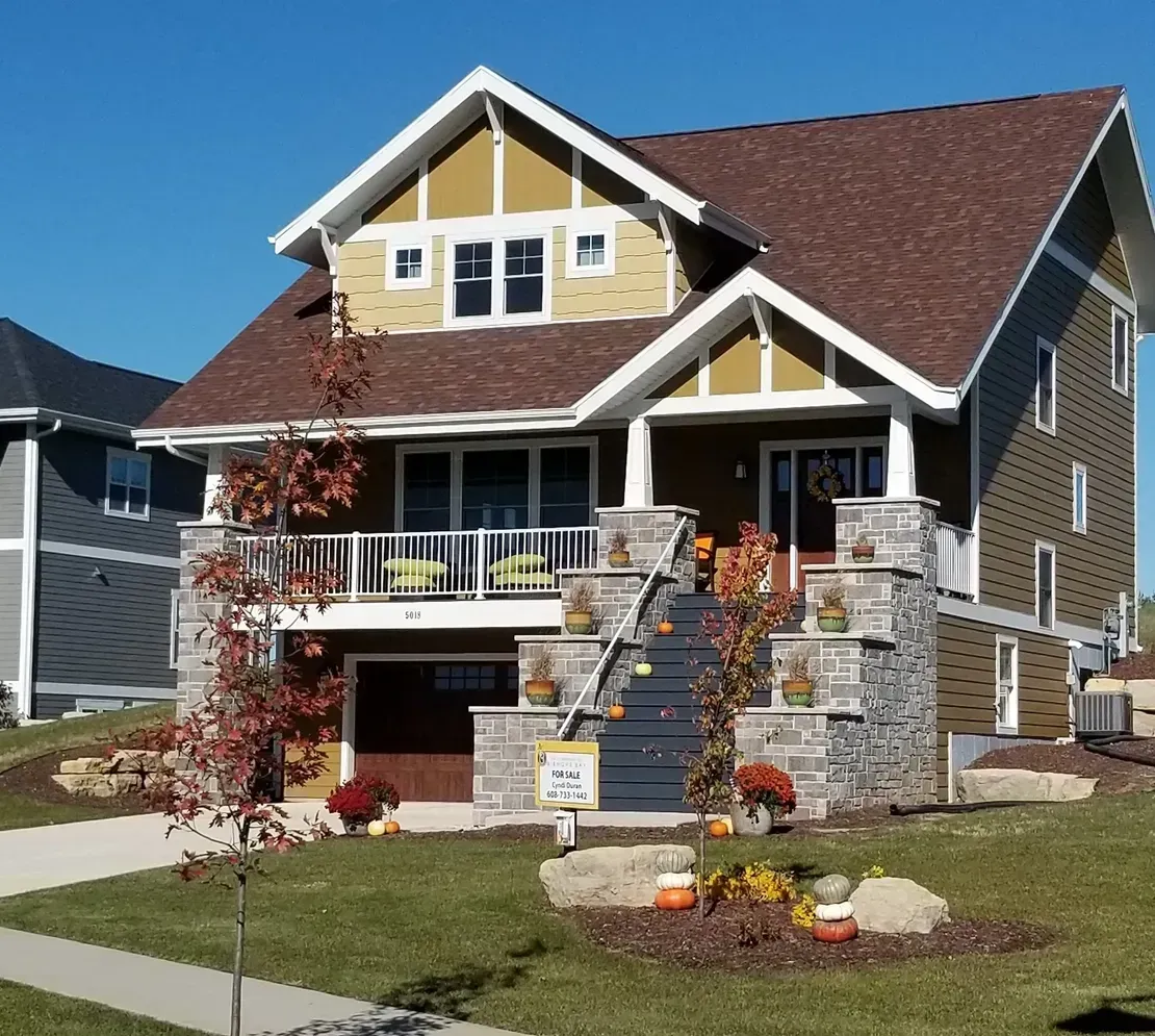 Two-story house with stone porch, red roof, and fall decorations on a suburban lawn
