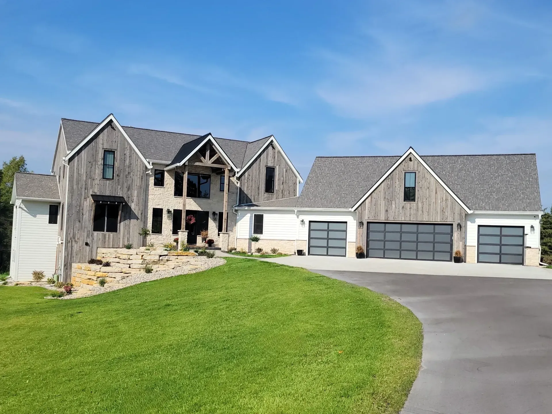 Large stone house with three-car garage and curved driveway under a blue sky