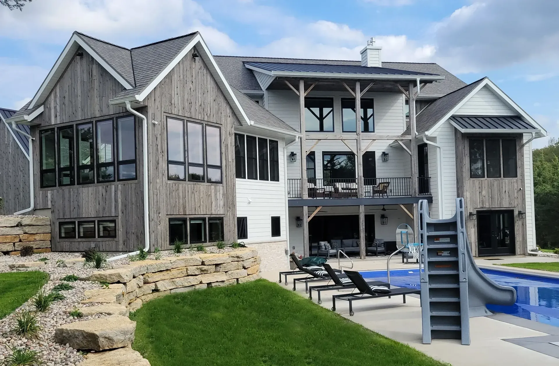Large waterfront house under construction with exposed framing, pool, and slide on a grassy lot