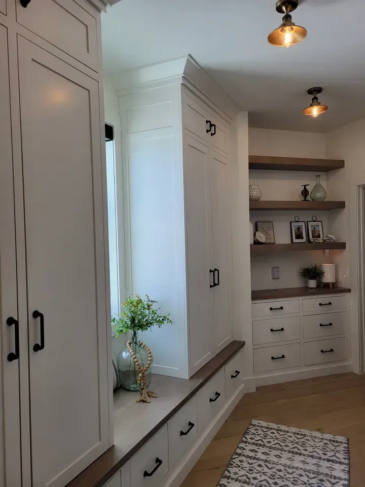 Built-in white cabinetry and shelving in a bright mudroom with black pulls and pendant lights