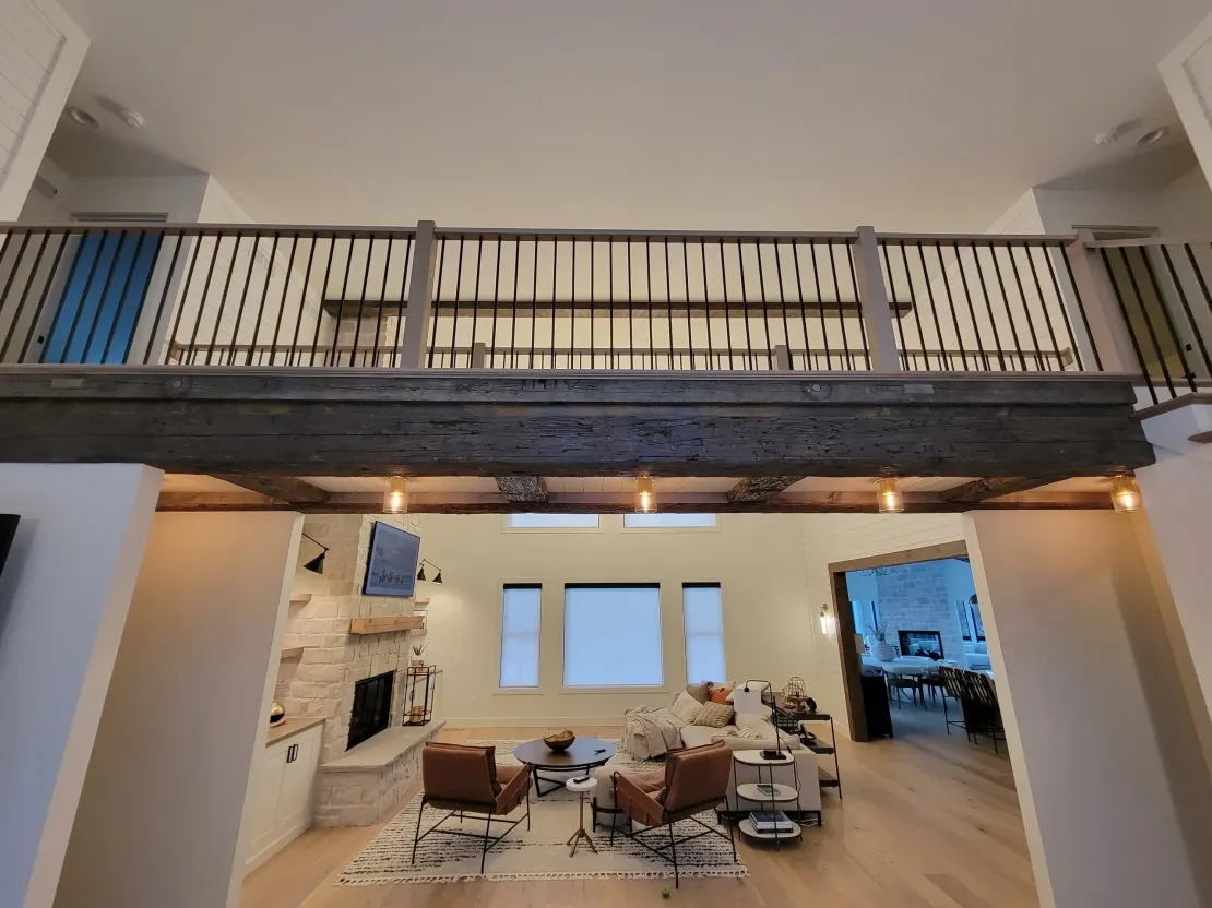Loft-style living room with wood floors, stone fireplace, and a balcony railing overhead