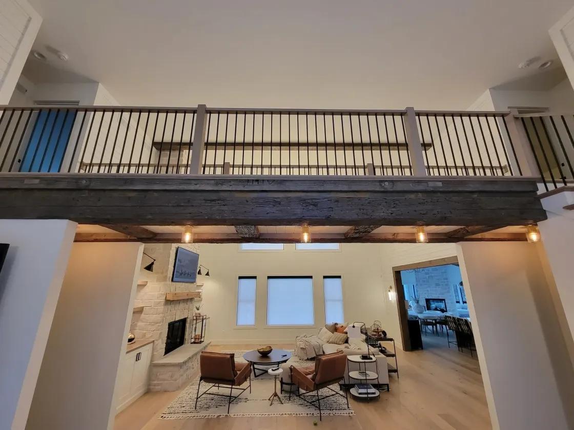 Modern loft living room with balcony railing, exposed stone wall, and warm wood floors