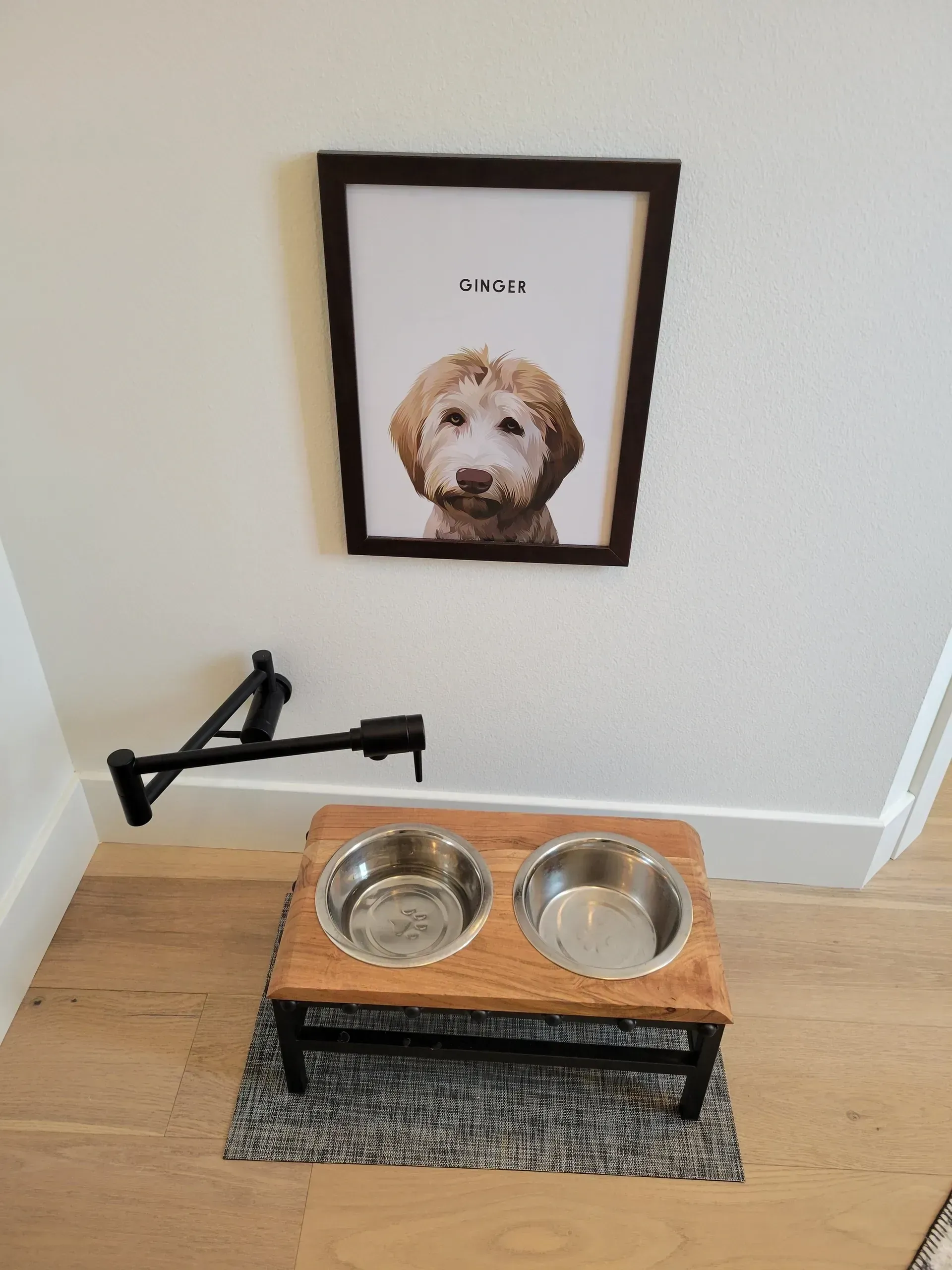 Dog portrait above two metal bowls on a wooden feeder in a corner by a wall-mounted leash hook.
