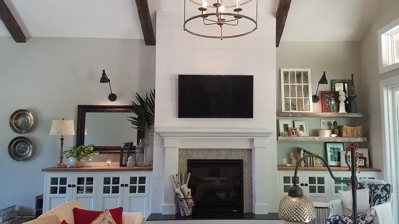Bright living room with a fireplace, wall-mounted TV, shelves, and decorative mirrors and lamps