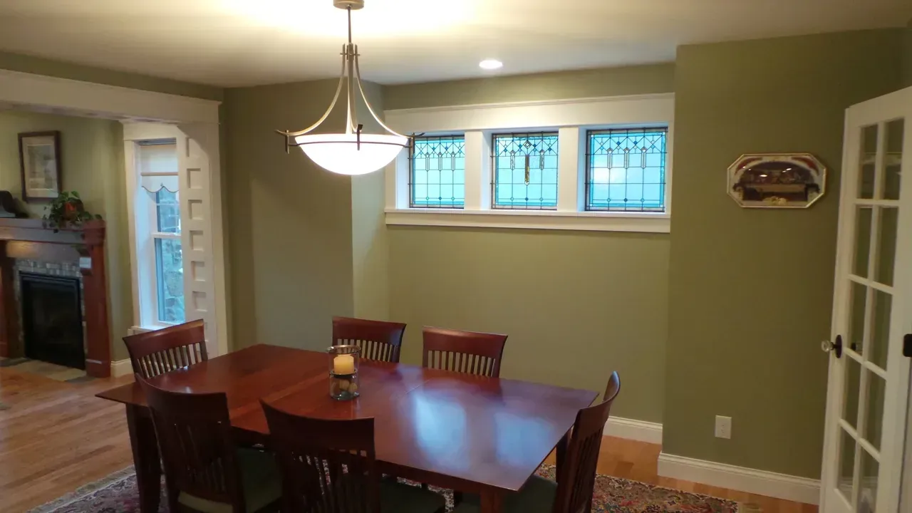 Dining room with wooden table and chairs, green walls, chandelier, and a small window above the baseboard heater