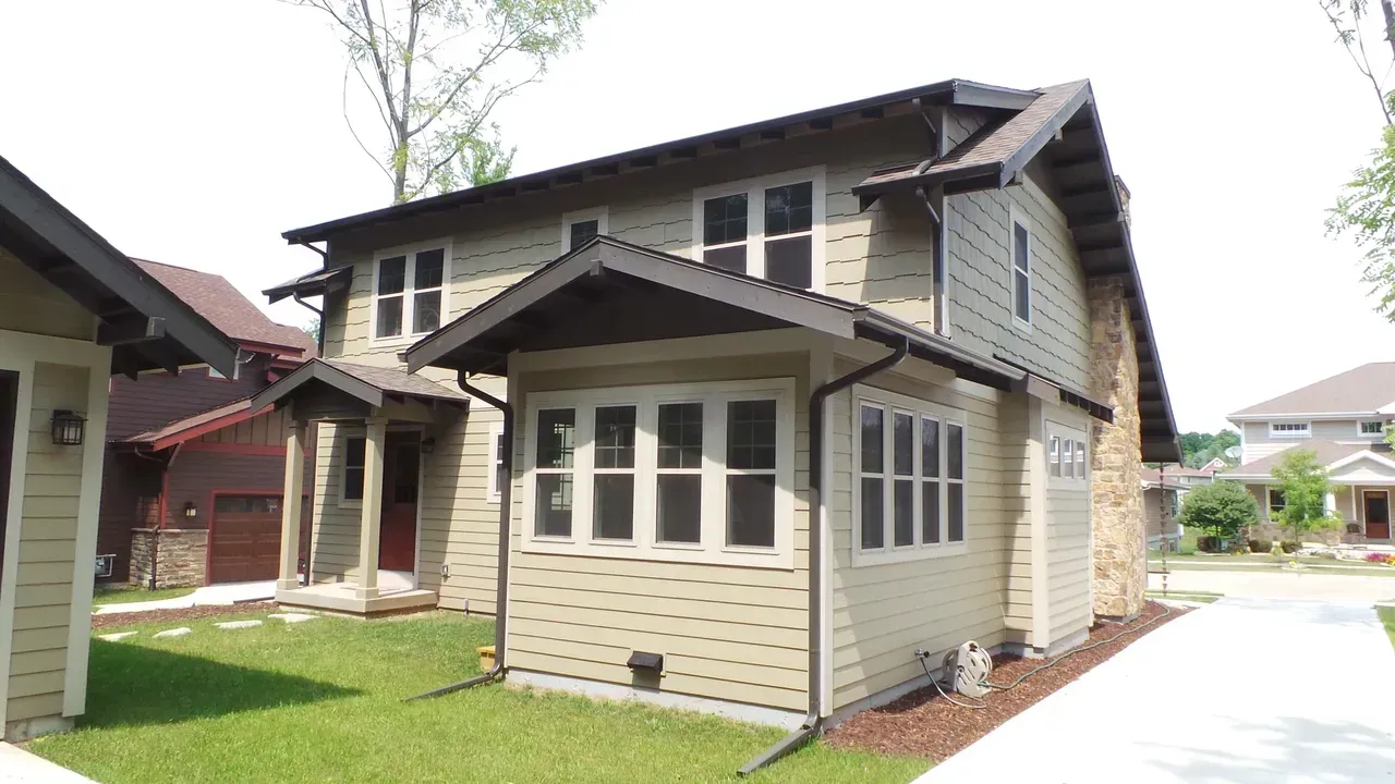 Two-story beige house with brown trim and a small covered porch in a suburban neighborhood