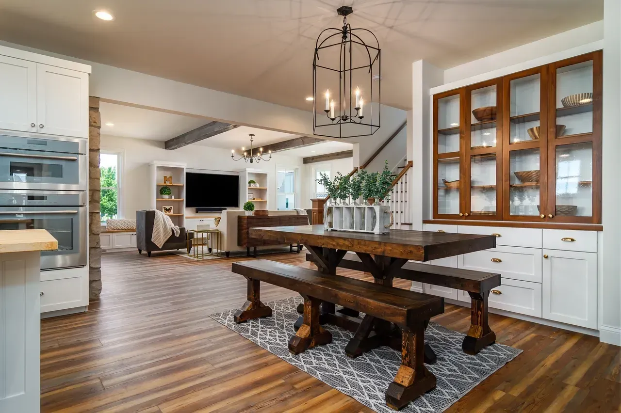 Bright farmhouse kitchen and dining area with wood table, bench seating, white cabinets, and glass hutch
