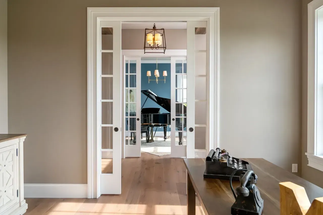 Bright hallway with French doors opening to a room where a grand piano sits near a window.