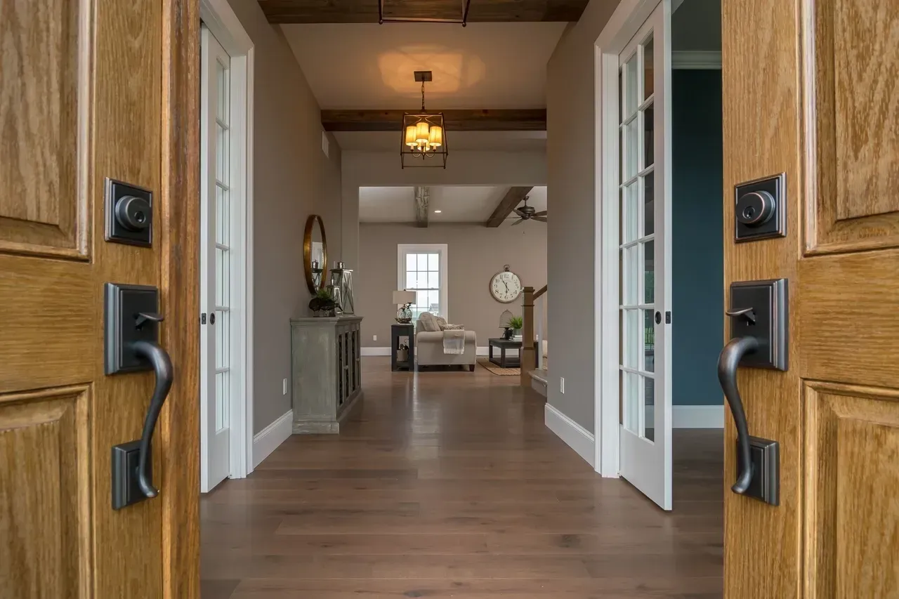 Open front doors looking into a warm, modern hallway and dining area with wood floors and neutral decor