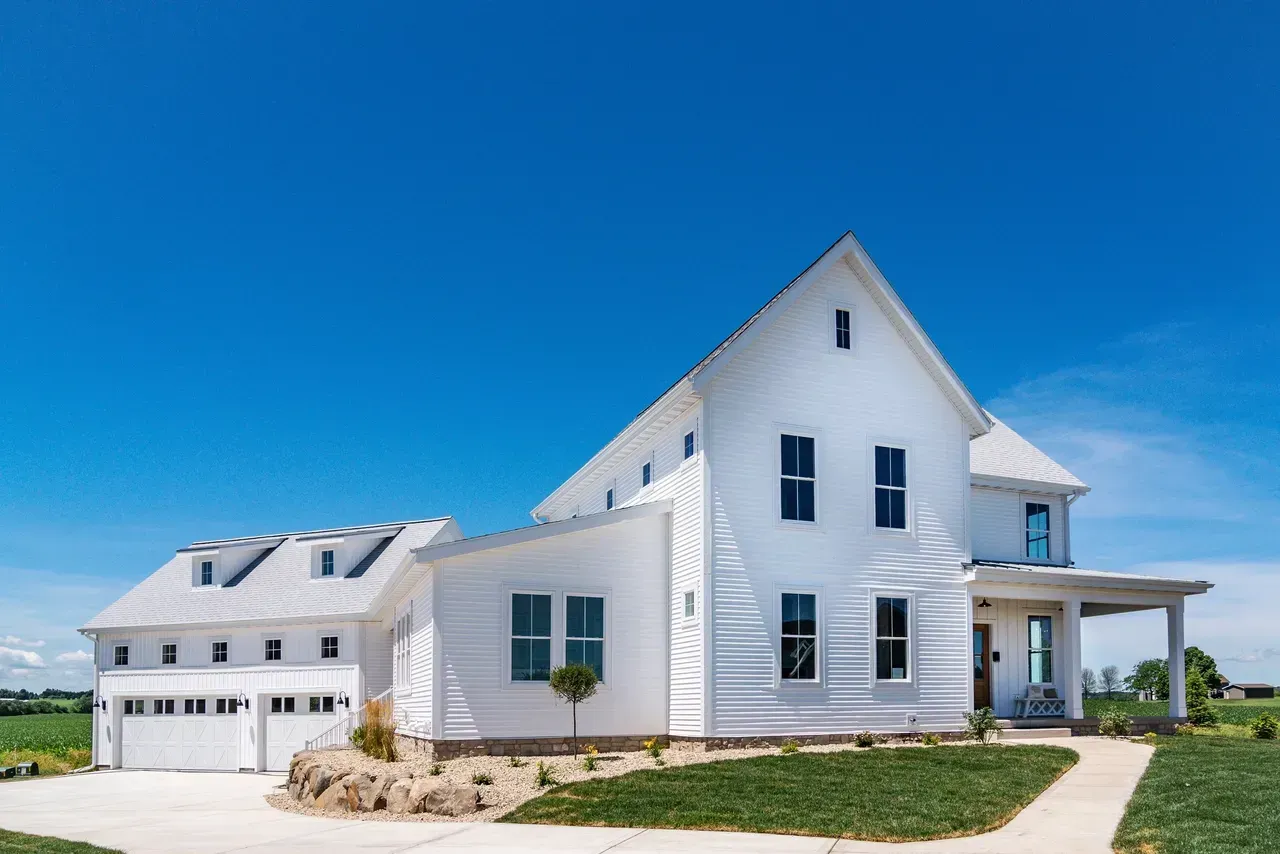White farmhouse with attached garage and porch under a clear blue sky