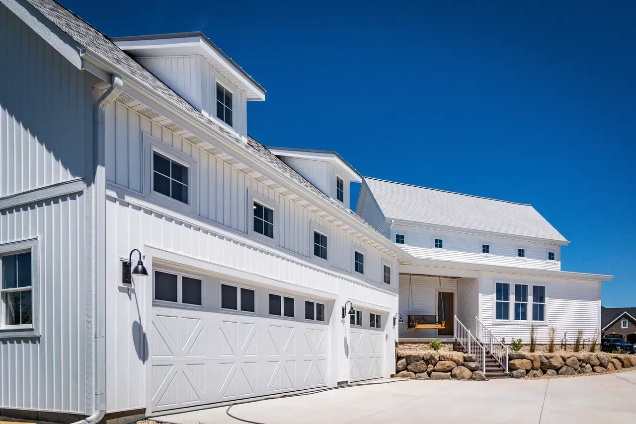 White barn-style building with garage doors and a small outdoor seating area under a bright blue sky