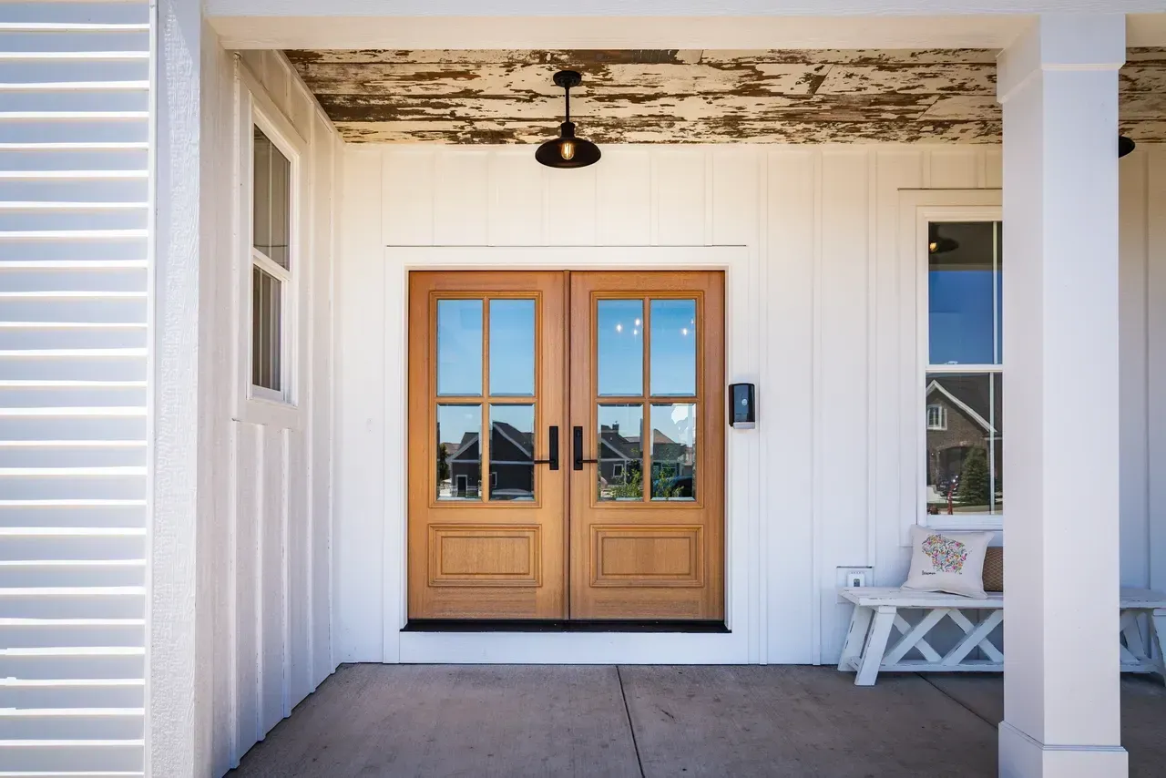 Front porch with tan double doors, white columns, and a bench beside a window.