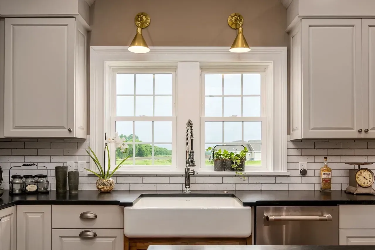 Bright kitchen with white cabinets, farmhouse sink, brass lights, and a window over the counter.
