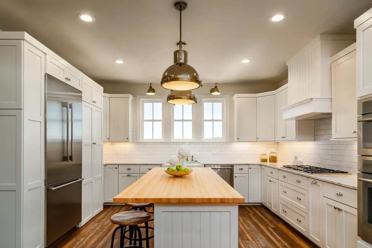 Bright modern white kitchen with island, stainless fridge, wood floors, and brass pendant lights
