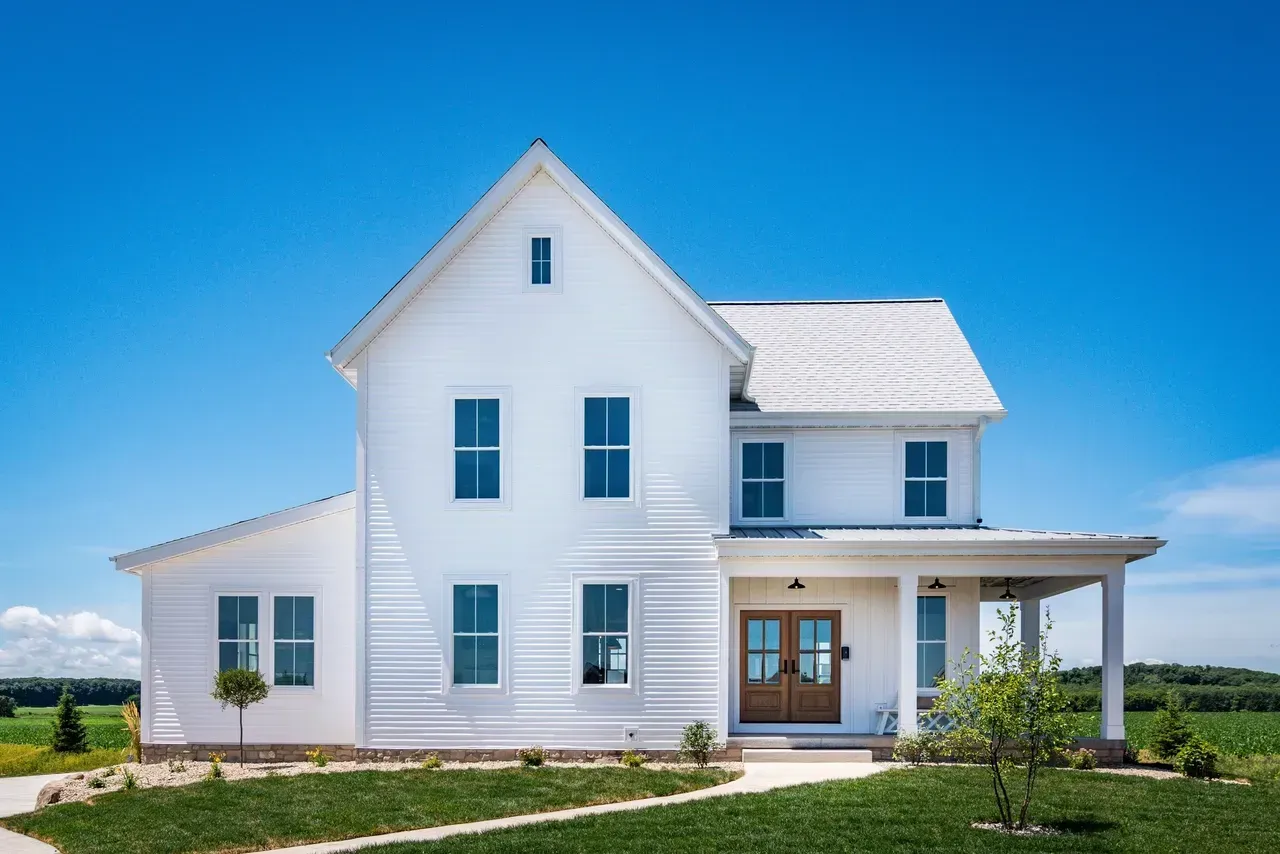 White two-story house with blue shutters and a front porch on a sunny day