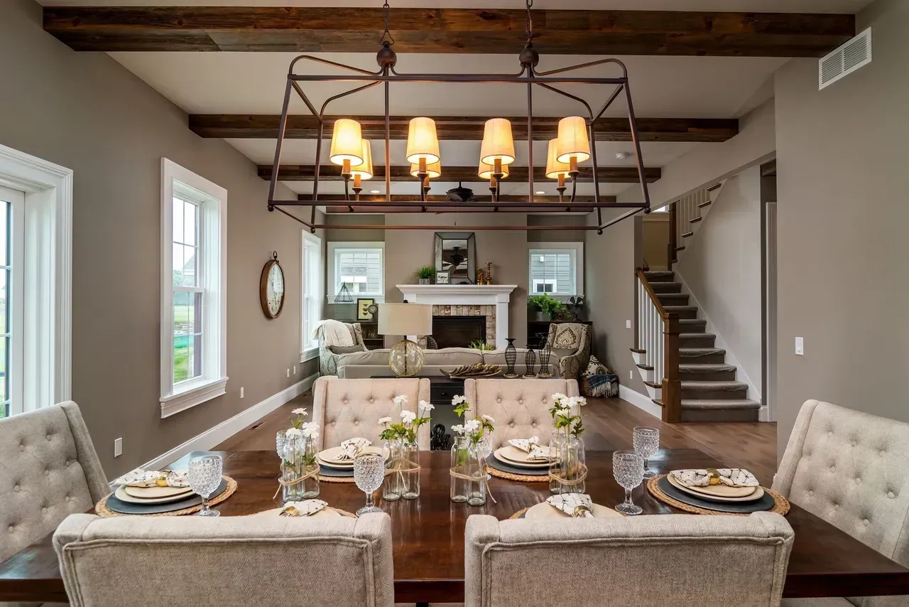 Elegant dining room with chandelier, long table set for a meal, fireplace, and staircase in a warm neutral interior