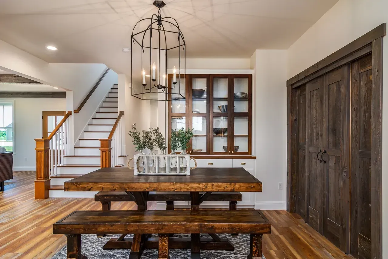 Rustic dining room with wooden table, bench, staircase, and large barn-style doors
