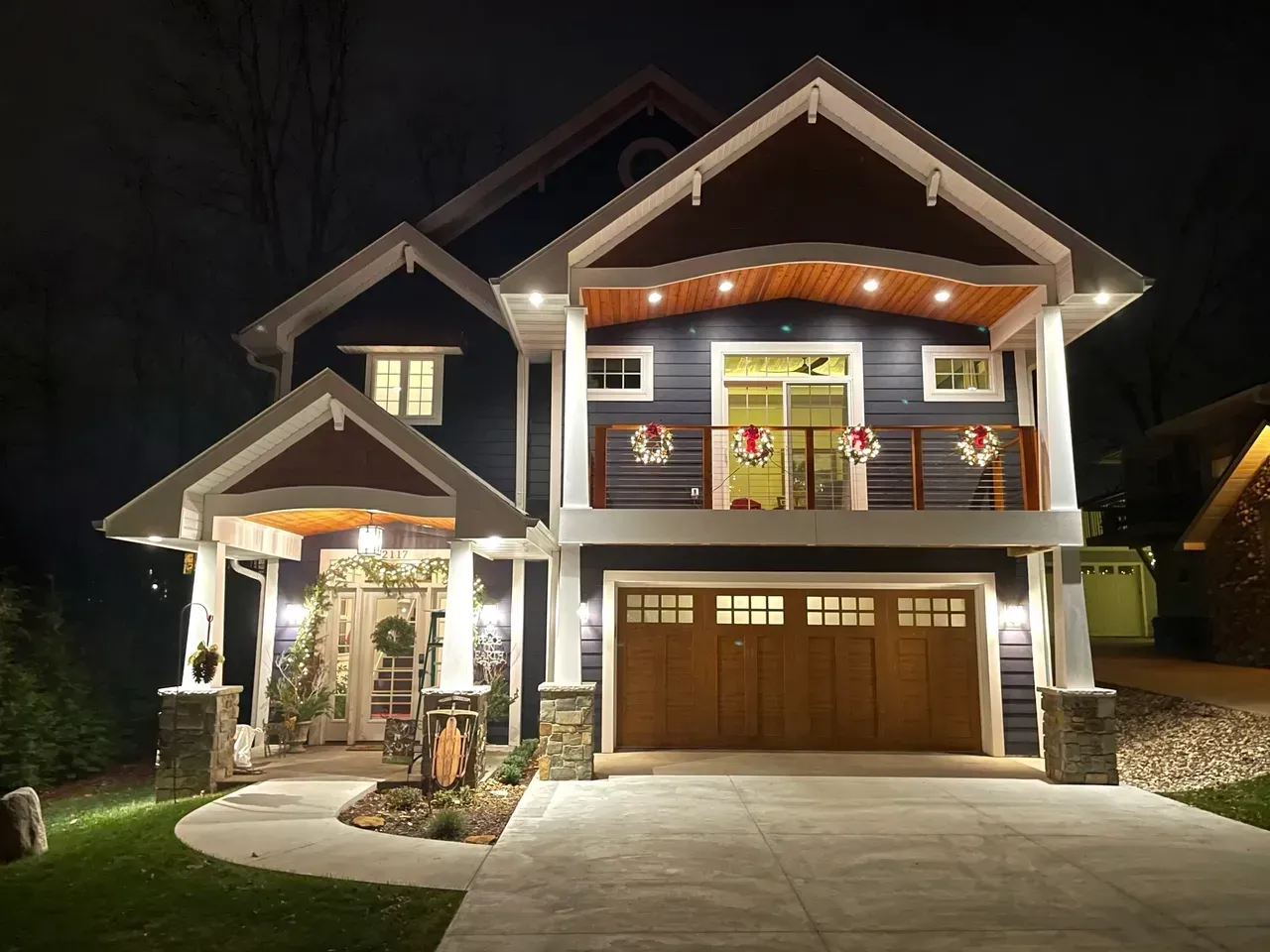 Two-story house at night with warm lights, front porch, balcony, and a double garage.