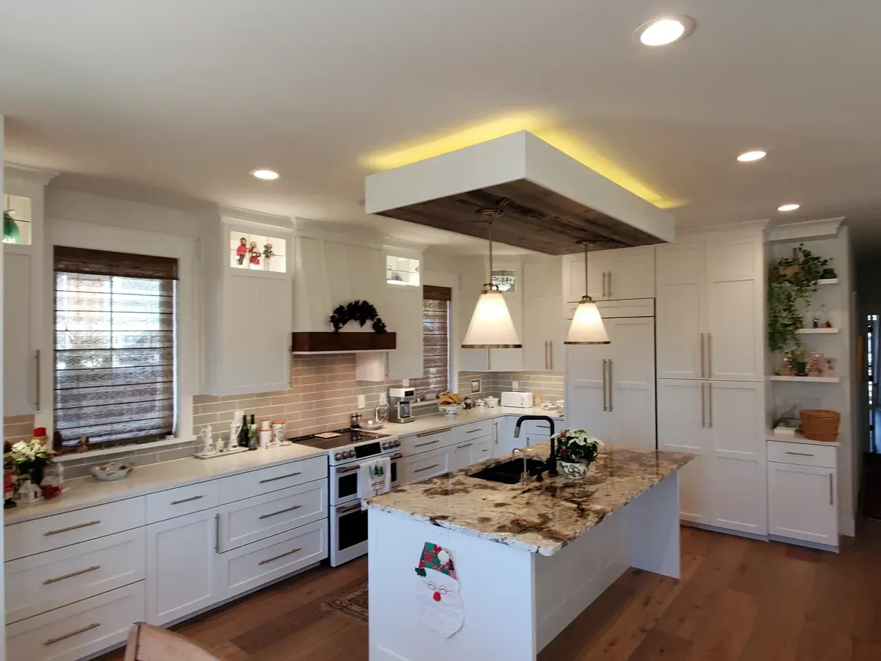 Bright white kitchen with granite island, pendant lights, built-in ovens, and large farmhouse sink.