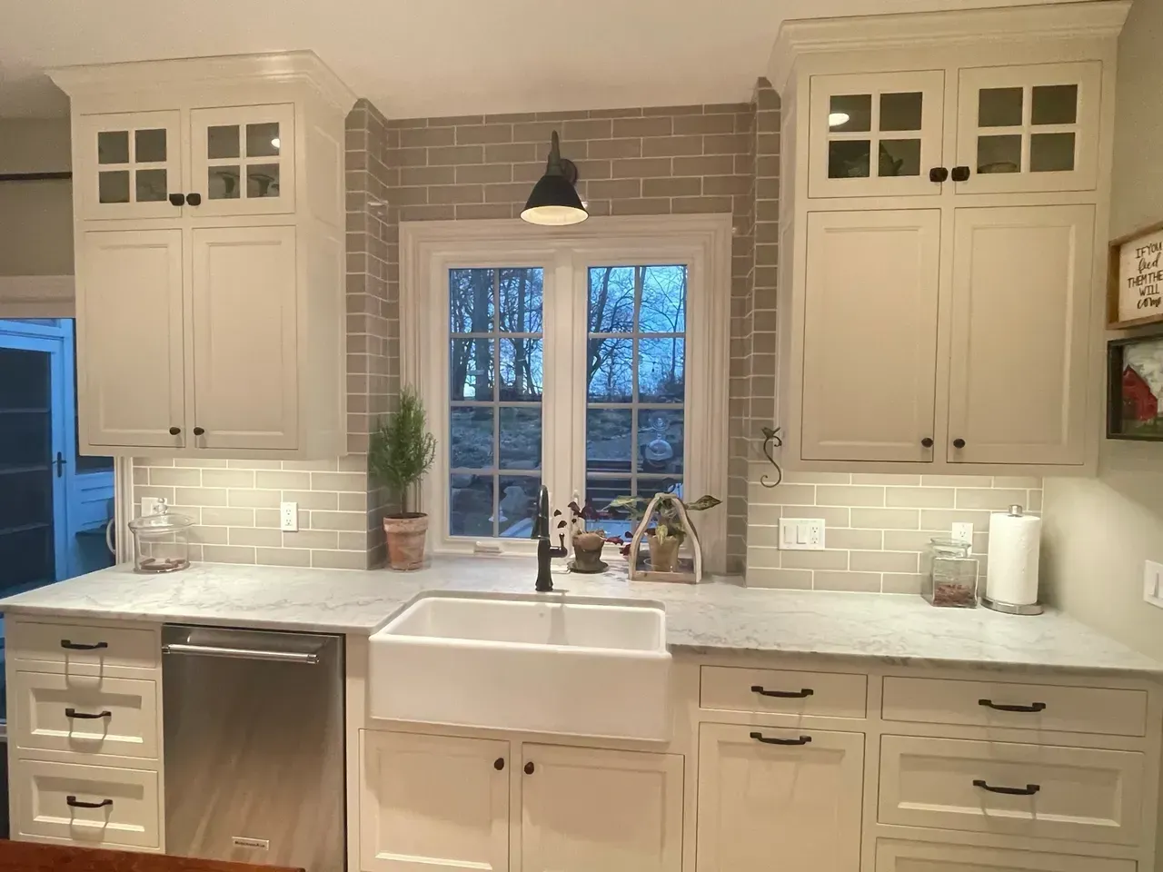 Bright white kitchen with farmhouse sink, marble backsplash, pendant light, and window above the sink