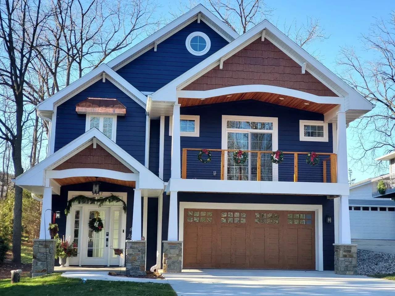 Modern two-story blue house with white trim, front porch, balcony, and brown garage door