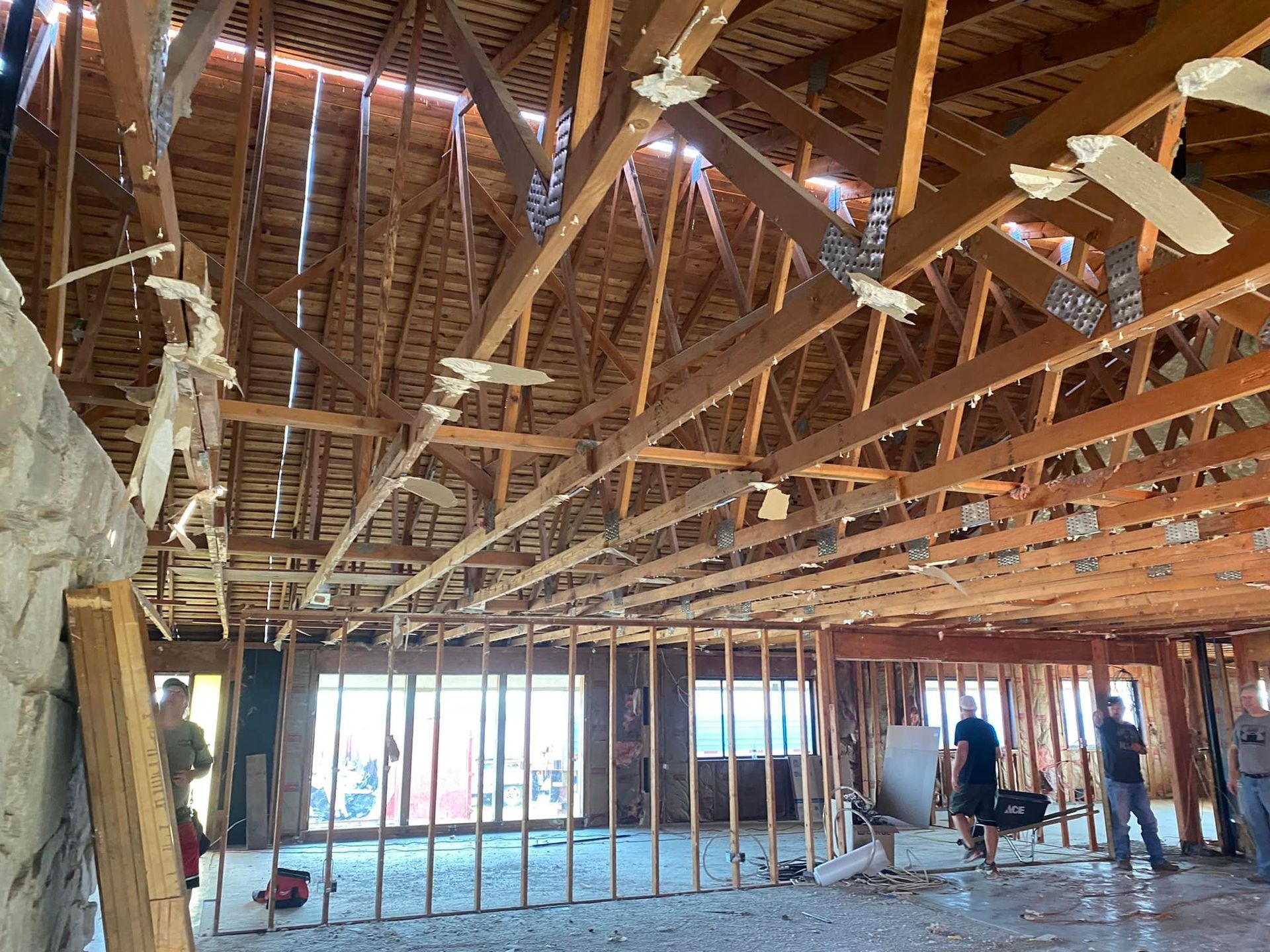 Exposed attic framing with workers installing ceiling pipes and drywall in a partly renovated room