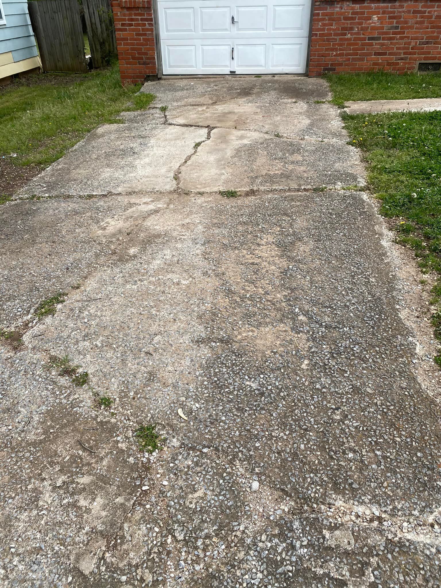 Cracked concrete driveway leading to a white garage door beside a brick house
