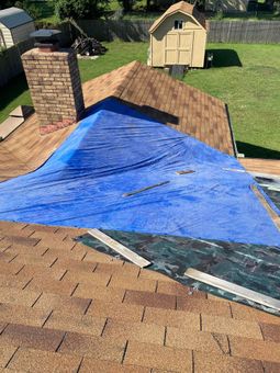 Blue tarp covering a damaged roof next to a brick chimney and garden shed