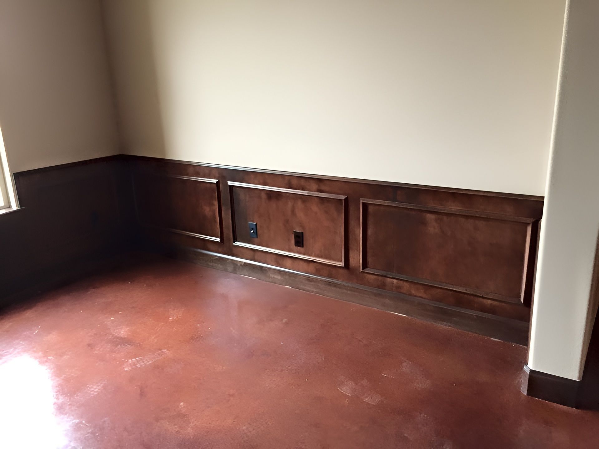 Empty room corner with wood-paneled walls and a reddish floor