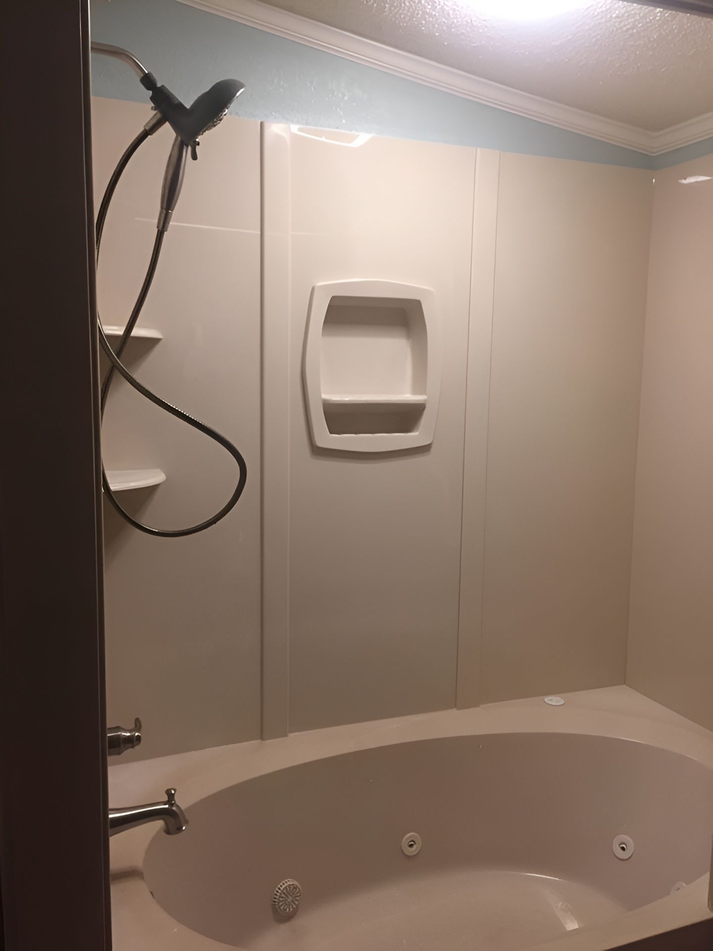 A beige bathroom with a jetted tub, handheld shower, and wall-mounted shelf.