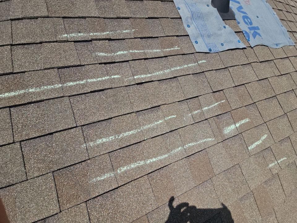 Rooftop shingles with chalk marking lines and a worker’s shadow in the foreground
