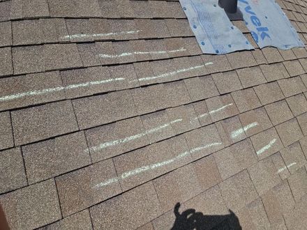Rooftop shingles with chalk marking lines and a worker’s shadow in the foreground